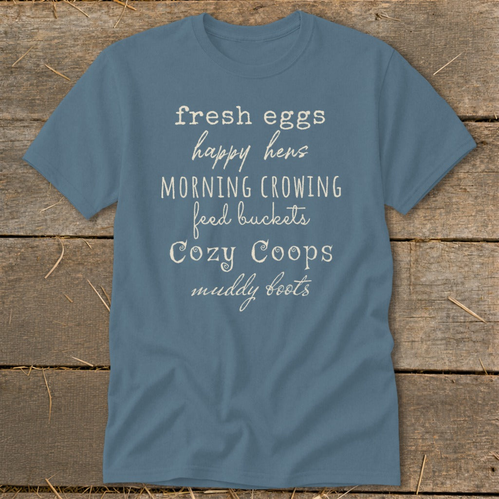 Blue t-shirt with white text listing "fresh eggs happy hens MORNING CROWING feed buckets Cozy Coops muddy boots".