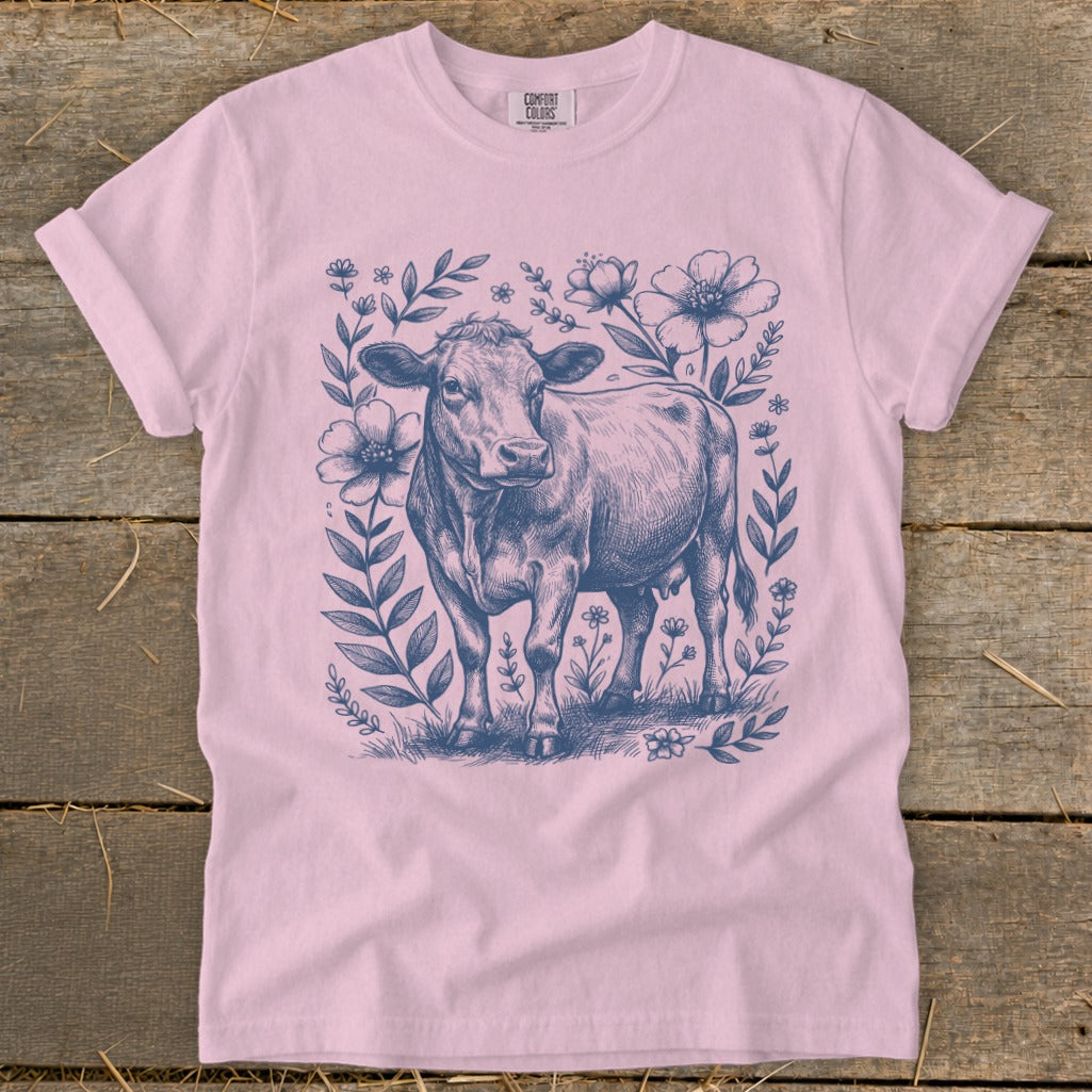 Pink t-shirt with a navy blue sketch of a cow surrounded by flowers and leaves.