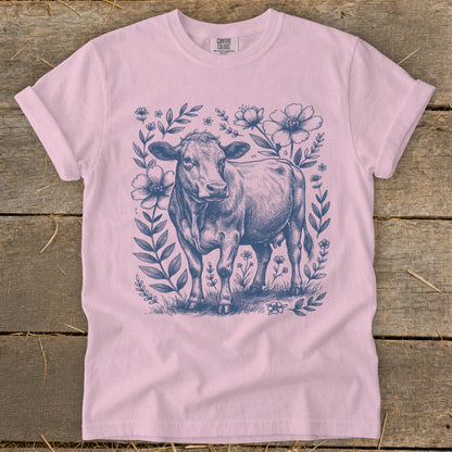 Pink t-shirt with a navy blue sketch of a cow surrounded by flowers and leaves.