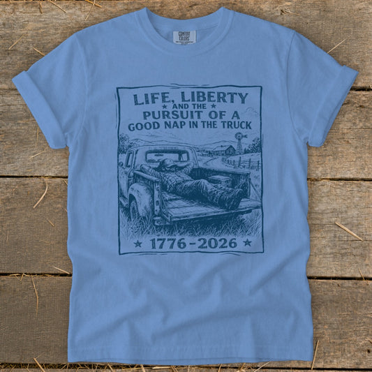 Blue t-shirt with black graphic of man napping in truck bed, reading "Life, Liberty and the Pursuit of a Good Nap in the Truck".