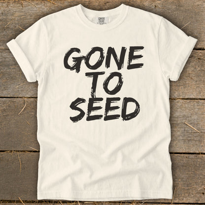 Cream t-shirt with black text "GONE TO SEED" on a wooden background.