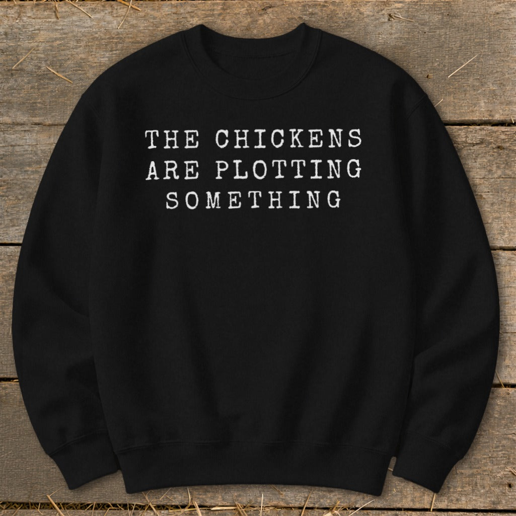 Black sweatshirt with white text reading "THE CHICKENS ARE PLOTTING SOMETHING."