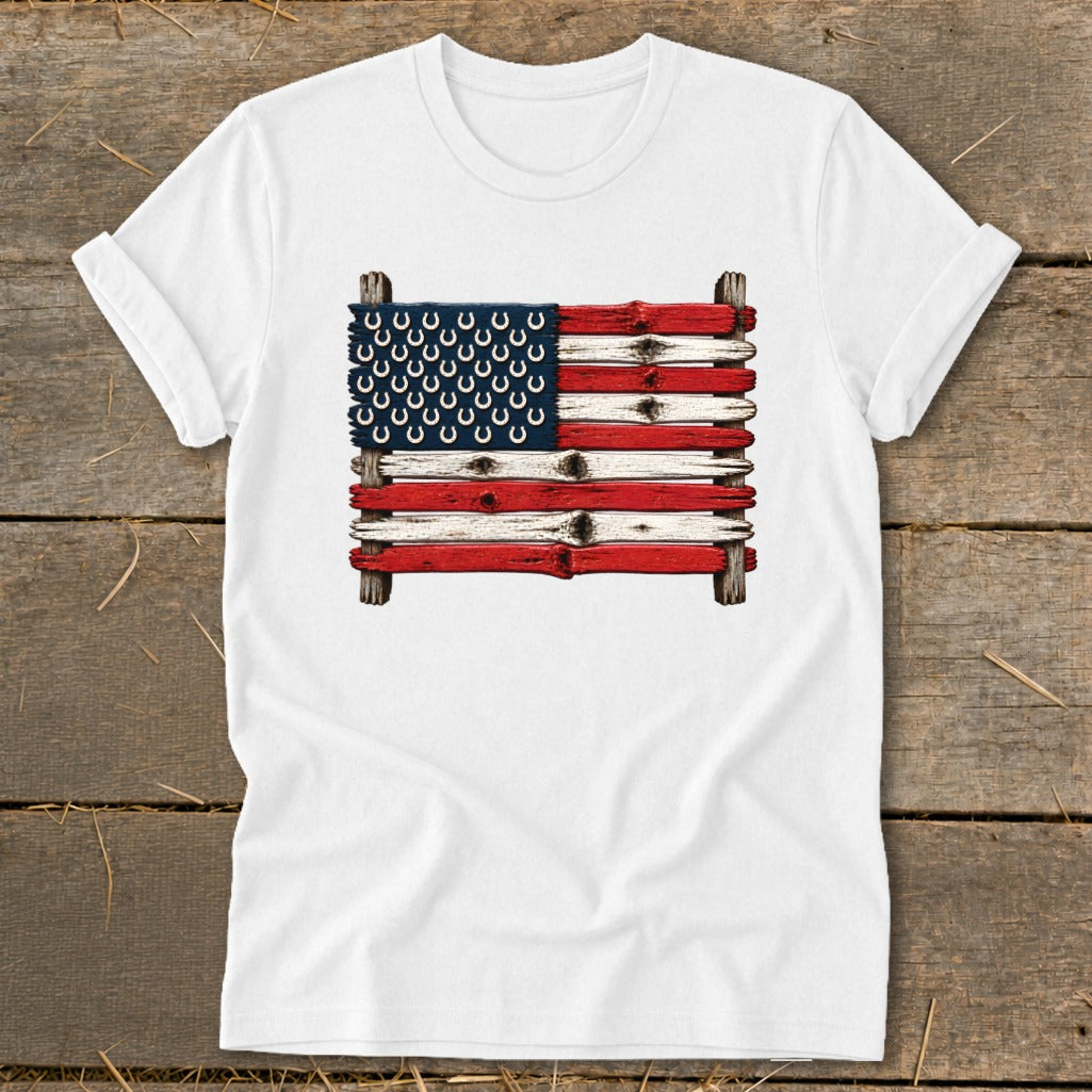 A white t-shirt featuring a rustic American flag graphic made of painted wooden planks and horseshoes.