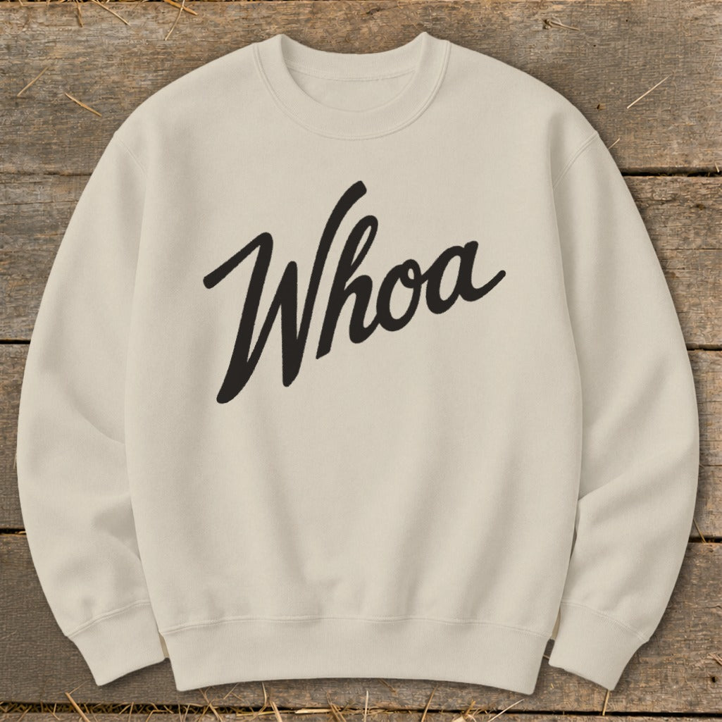 Cream sweatshirt with black "Whoa" text on a wooden background.