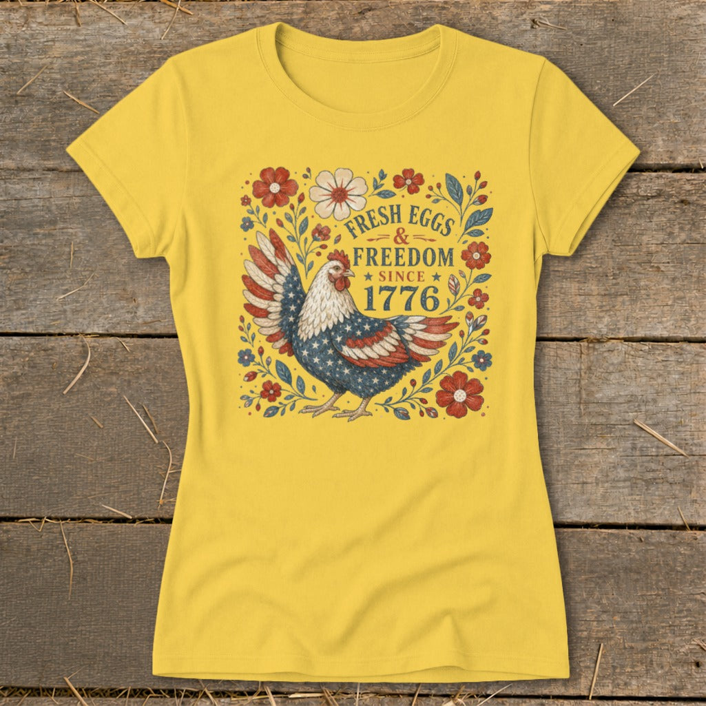 Chicken graphic with American flag wings on a yellow t-shirt, text reads "Fresh Eggs & Freedom Since 1776".