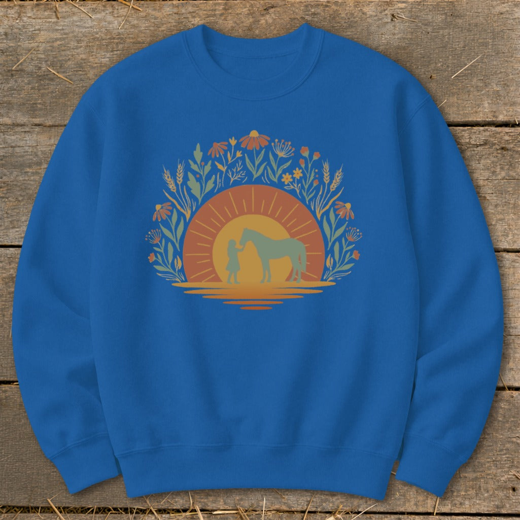 Blue sweatshirt with a graphic of a person and horse at sunset surrounded by flowers.