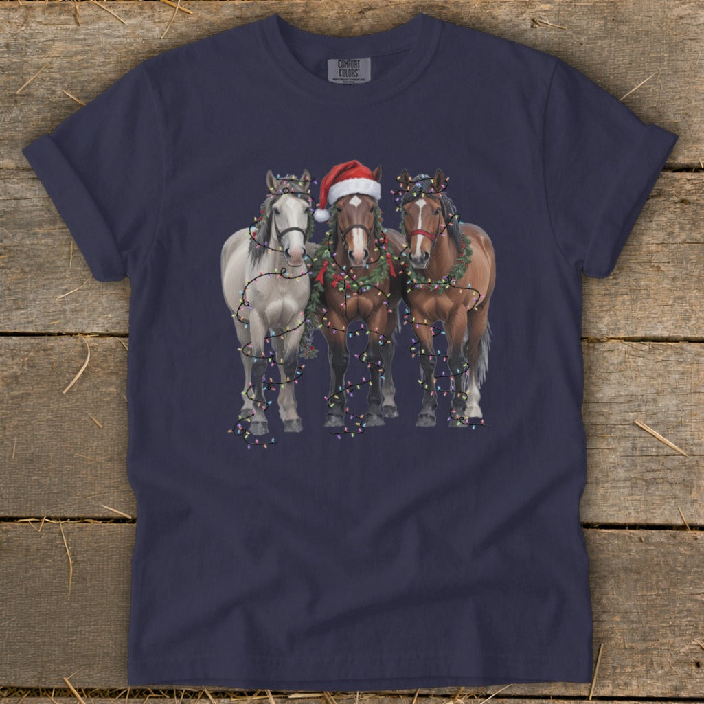 Three horses wearing Christmas lights and wreaths, one with a Santa hat.