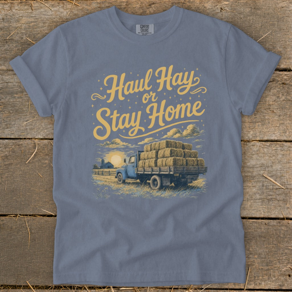 Blue t-shirt featuring a graphic of a blue truck loaded with hay bales and text "Haul Hay or Stay Home".