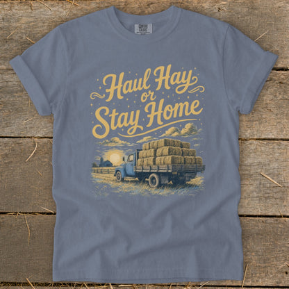 Blue t-shirt featuring a graphic of a blue truck loaded with hay bales and text "Haul Hay or Stay Home".