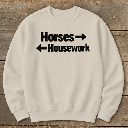 Cream-colored crewneck sweatshirt with black text reading Horses with a right arrow and Housework with a left arrow.