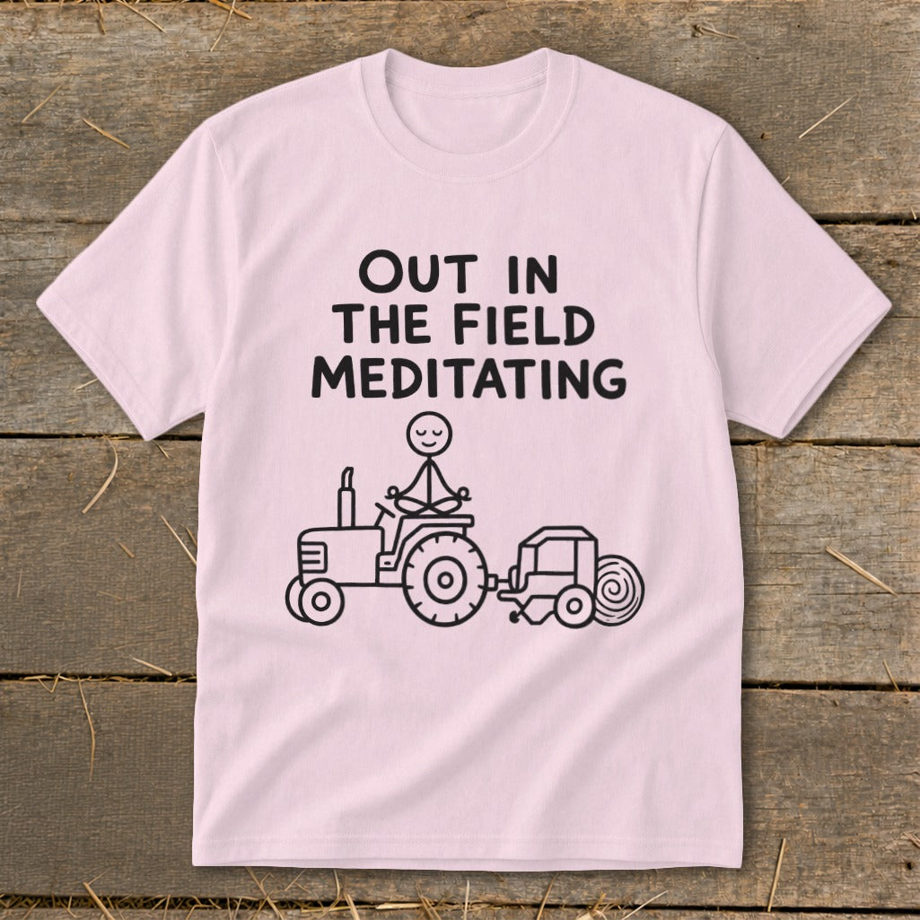 Pink t-shirt with black text "OUT IN THE FIELD MEDITATING" and a stick figure on a tractor.