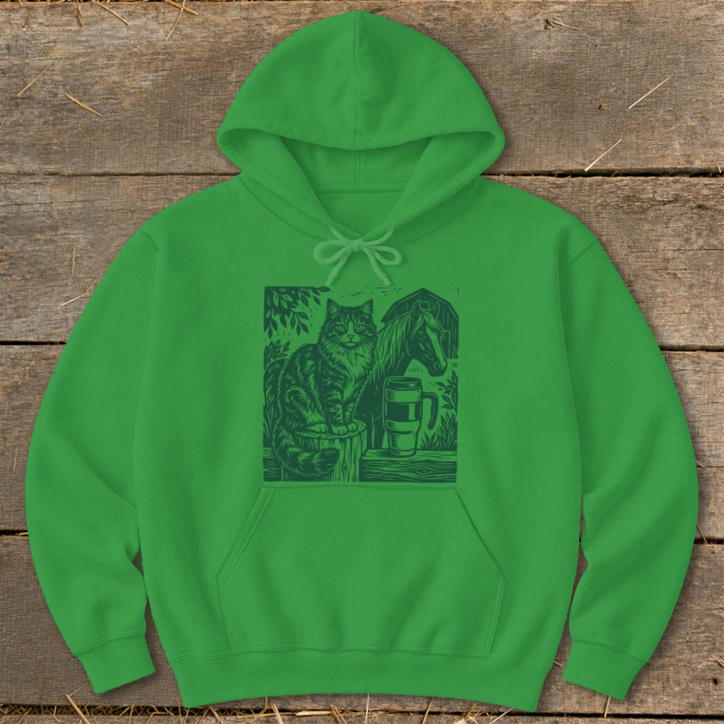 Green hoodie with a linocut print of a cat, horse, barn, and mug.