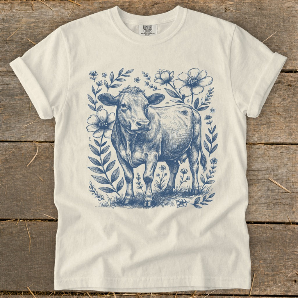 T-shirt with blue sketch of cow amidst flowers and foliage.