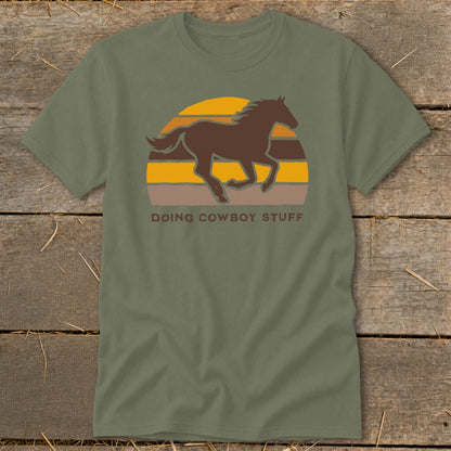 Green t-shirt with running horse and sunset graphic, text reads "Doing Cowboy Stuff".