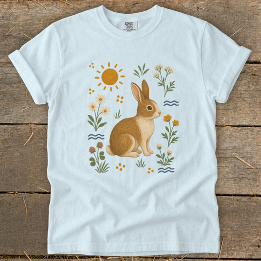 Light blue t-shirt with a brown rabbit surrounded by flowers, sun, and waves.