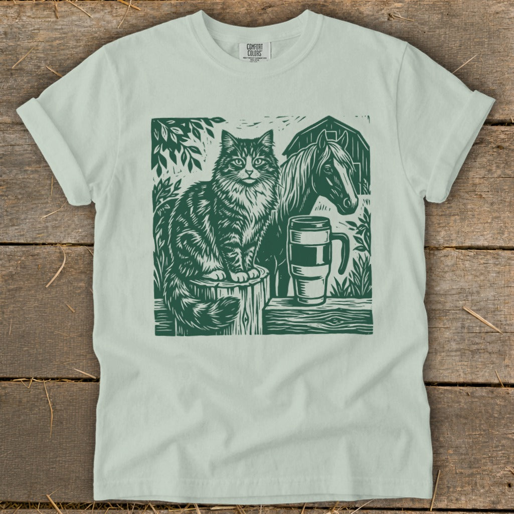 Cat and horse linocut print on a light green t-shirt with barn and mug.