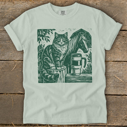 Cat and horse linocut print on a light green t-shirt with barn and mug.