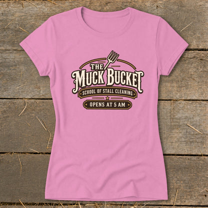 Pink t-shirt with "The Muck Bucket School of Stall Cleaning Opens at 5 AM" logo.