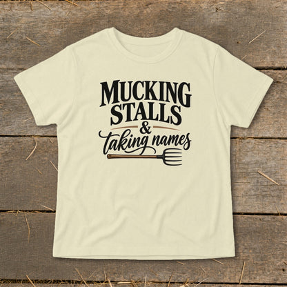 Cream t-shirt with black text reading "MUCKING STALLS & taking names" and a pitchfork graphic.