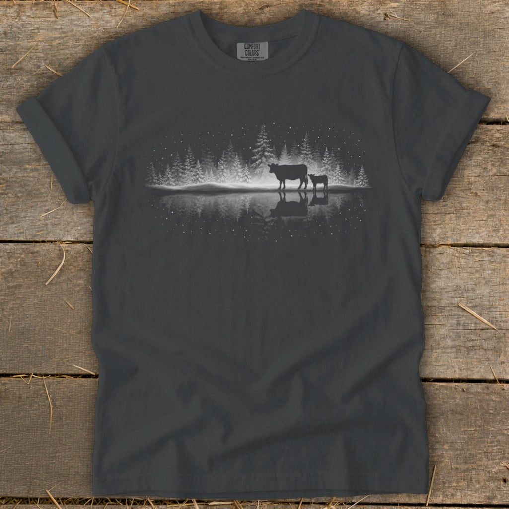 Silhouettes of two cows reflected in water with snowy trees and starry sky.