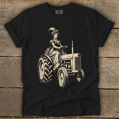 Black t-shirt with a sepia illustration of a woman in Victorian attire driving a tractor.