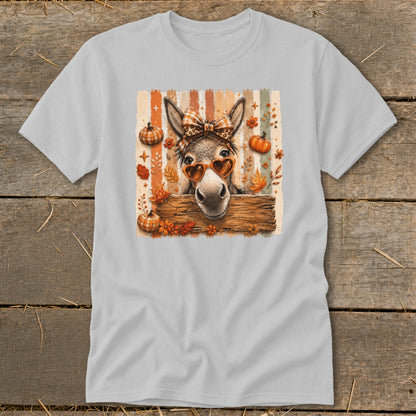 Donkey wearing heart sunglasses and bow peeking over wooden fence, with pumpkins and leaves.