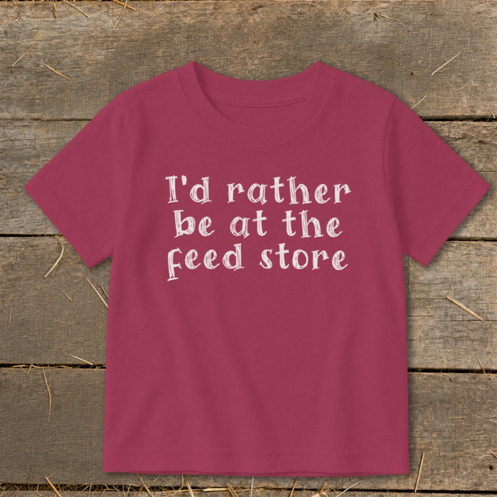 Pink t-shirt with white text: "I'd rather be at the feed store".