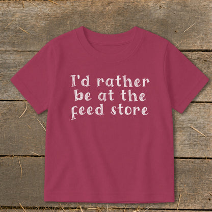 Pink t-shirt with white text: "I'd rather be at the feed store".