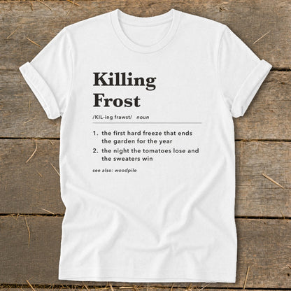 A white t-shirt with black text defining the term Killing Frost, laid flat on a rustic wooden background.