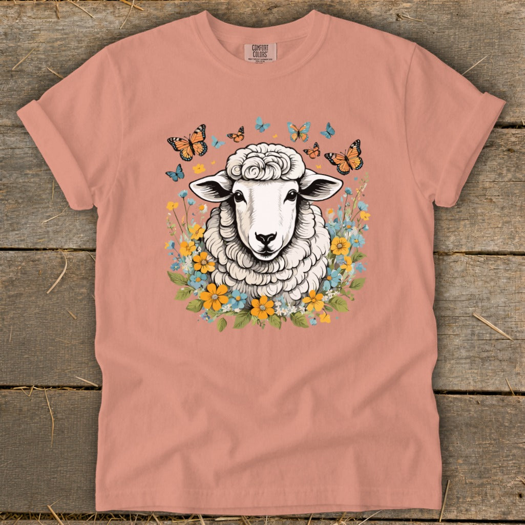 Fluffy sheep with butterflies and flowers graphic on a peach t-shirt.