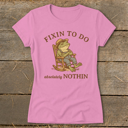 Pink t-shirt with a frog in overalls and hat on a rocking chair, "Fixin to do absolutely nothin" text.