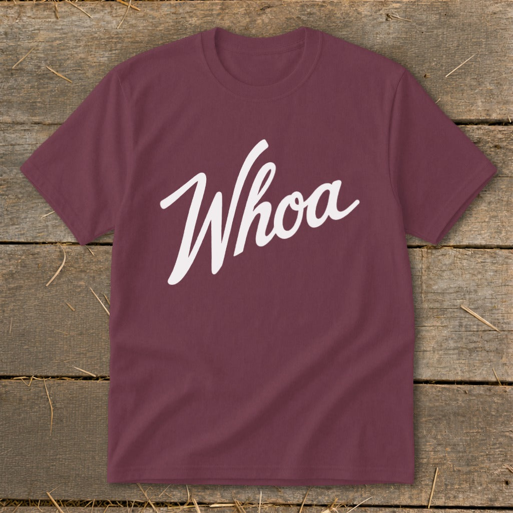 Maroon t-shirt with white cursive "Whoa" graphic on a rustic wooden background.