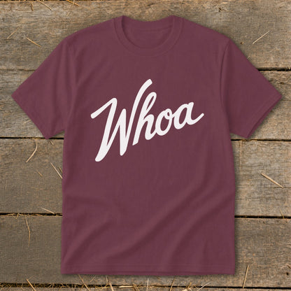 Maroon t-shirt with white cursive "Whoa" graphic on a rustic wooden background.