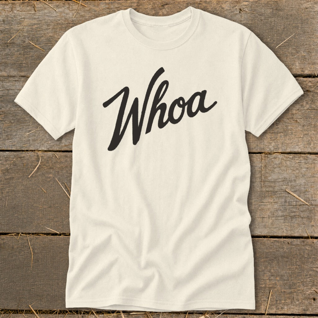 Cream t-shirt with "Whoa" in black script text on a wooden background.