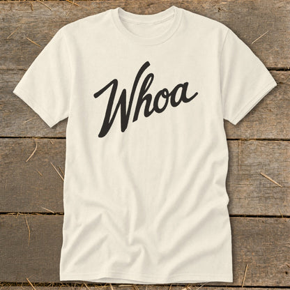 Cream t-shirt with "Whoa" in black script text on a wooden background.