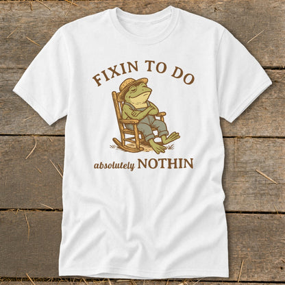 White t-shirt with graphic of frog in rocking chair and text "Fixin to do absolutely nothin".