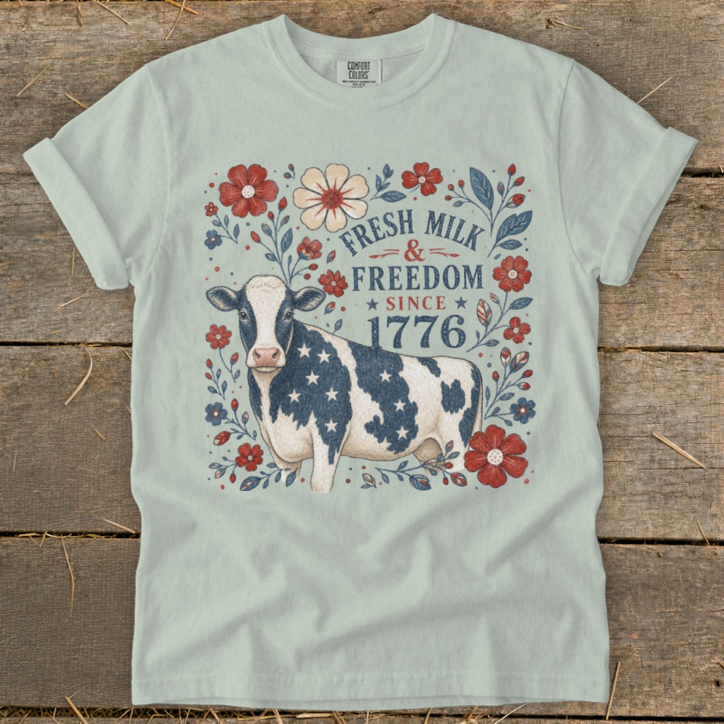 Cow with American flag stars on shirt surrounded by flowers, reads "Fresh Milk & Freedom Since 1776".