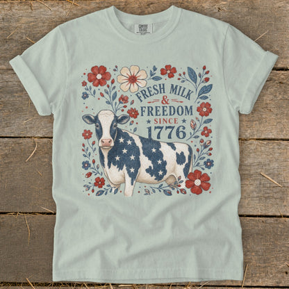 Cow with American flag stars on shirt surrounded by flowers, reads "Fresh Milk & Freedom Since 1776".