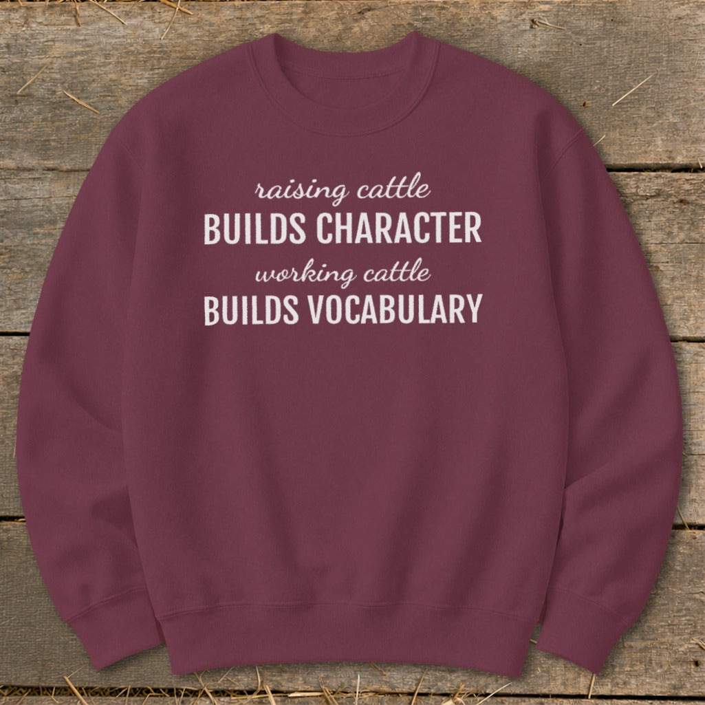 Maroon sweatshirt with white text: "raising cattle BUILDS CHARACTER, working cattle BUILDS VOCABULARY".
