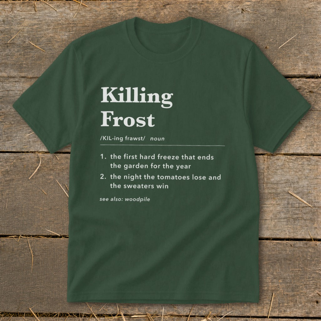Forest green t-shirt featuring white text that defines killing frost humorously, displayed on rustic wood.