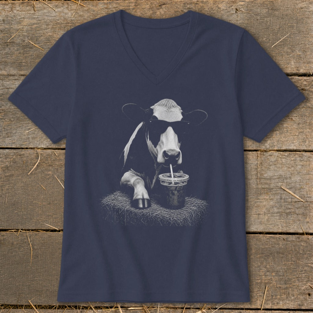 Cow wearing sunglasses drinks from a cup with a straw on a bale of hay.