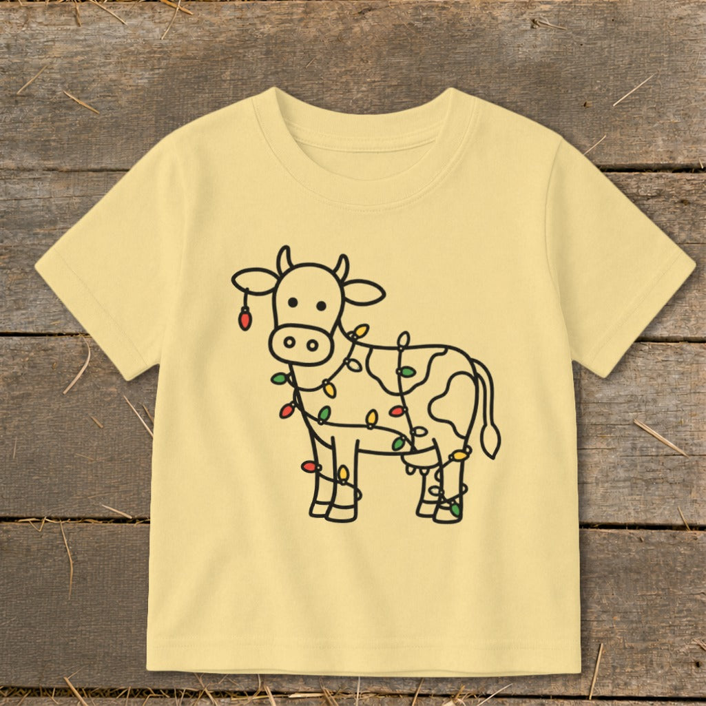 Light yellow t-shirt with a black line drawing of a cow wrapped in colorful Christmas lights.