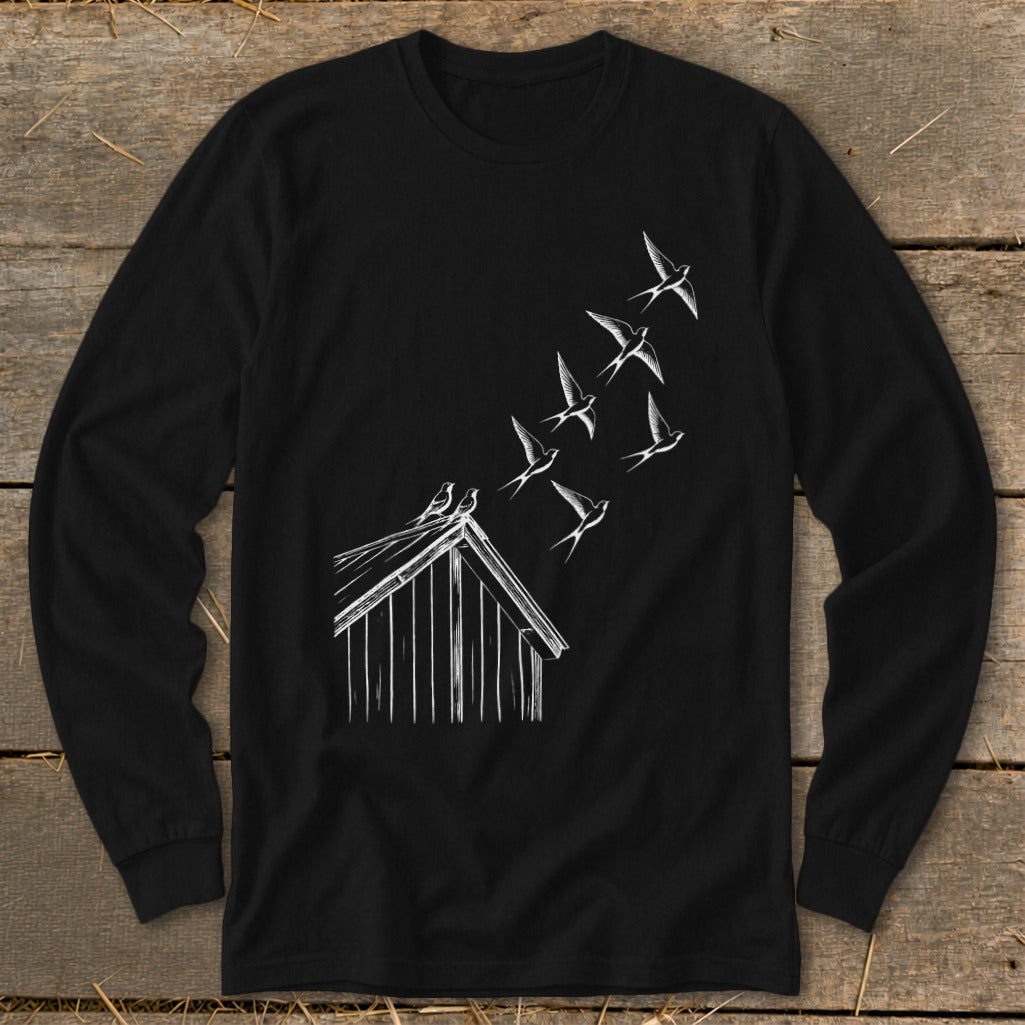 A black long-sleeve t-shirt with a white line art graphic of birds flying from a rustic wooden barn.