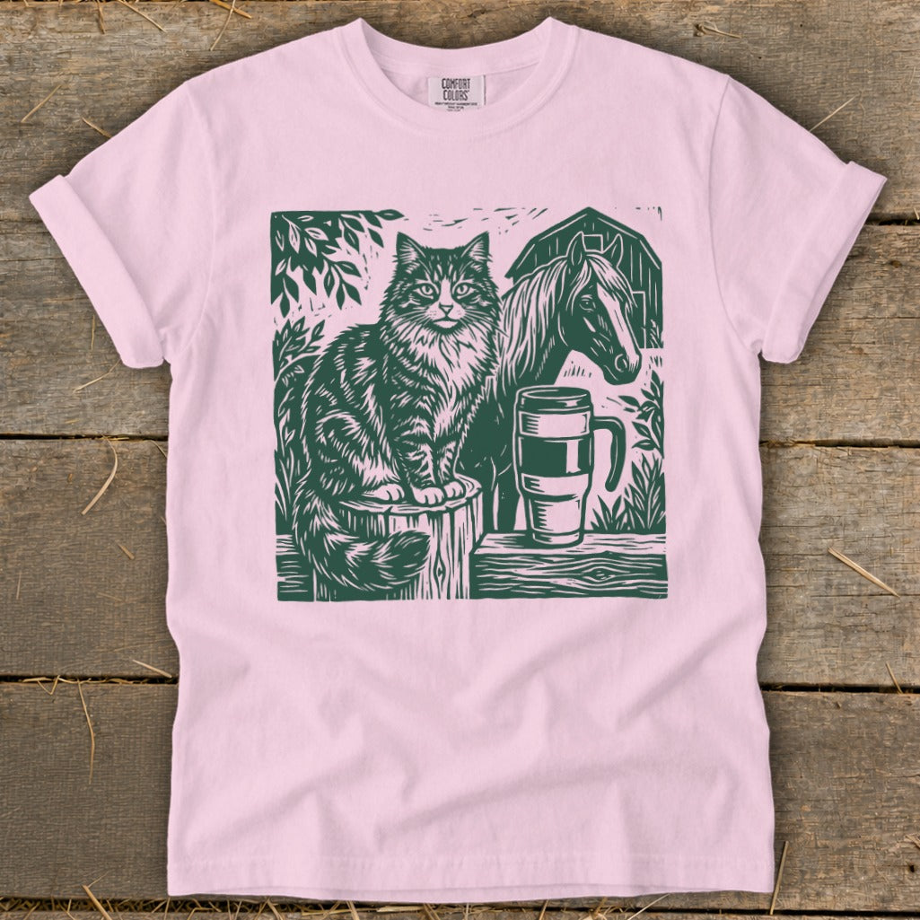 Cat, horse, and mug on a wooden surface with a barn and trees in the background.