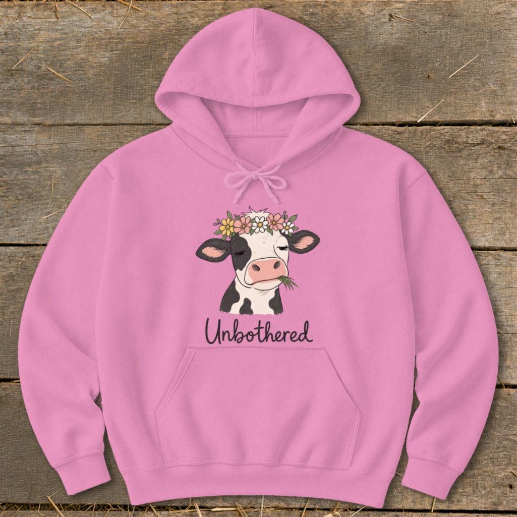 Pink hoodie with a black and white cow wearing a flower crown and eating grass, text says "Unbothered".
