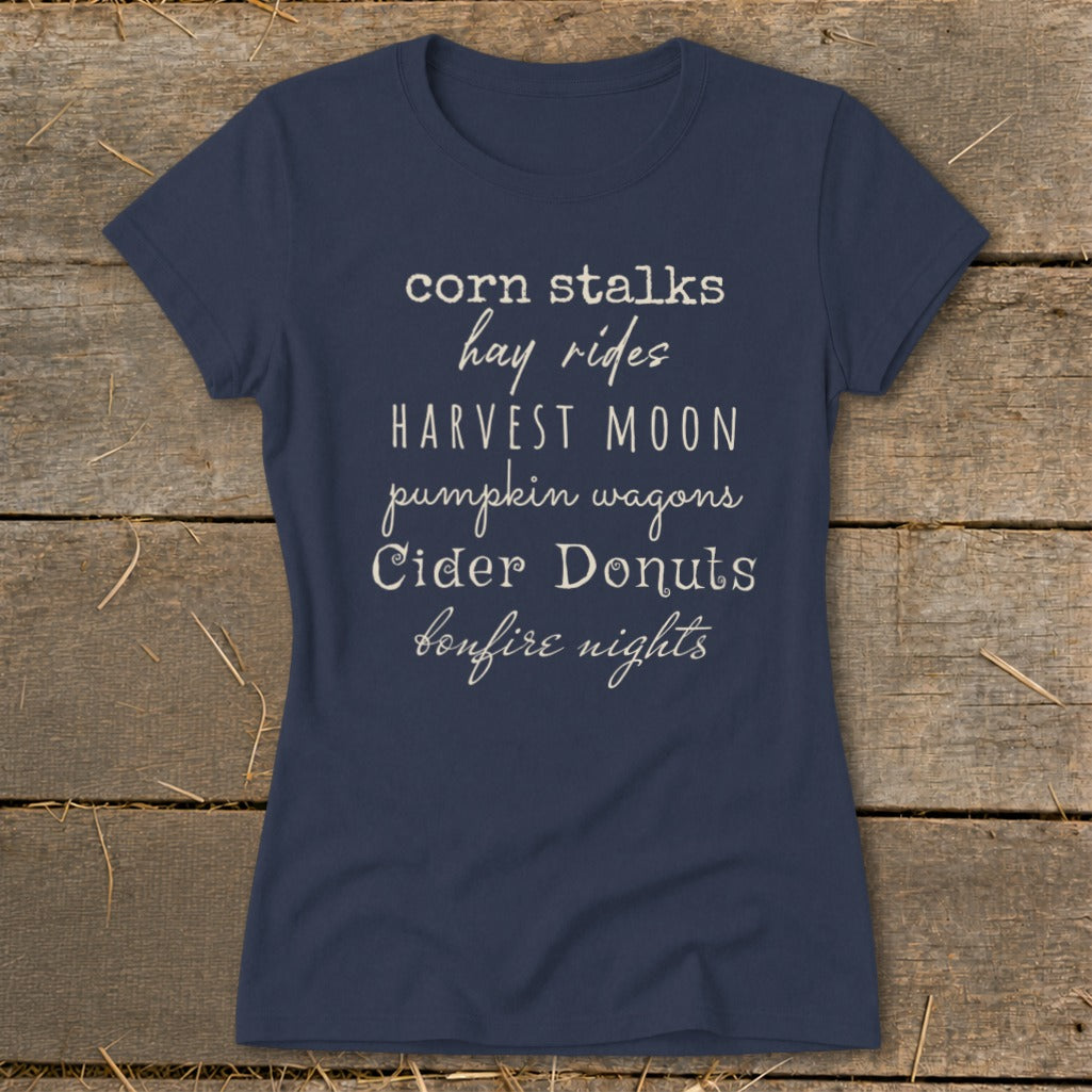 Navy t-shirt with fall-themed text: corn stalks, hay rides, harvest moon, pumpkin wagons, cider donuts, bonfire nights.