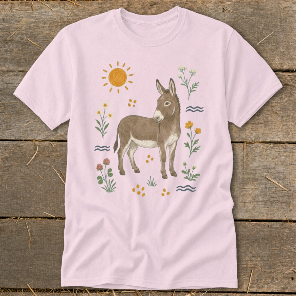 Light pink t-shirt with a watercolor illustration of a donkey surrounded by flowers and a sun.