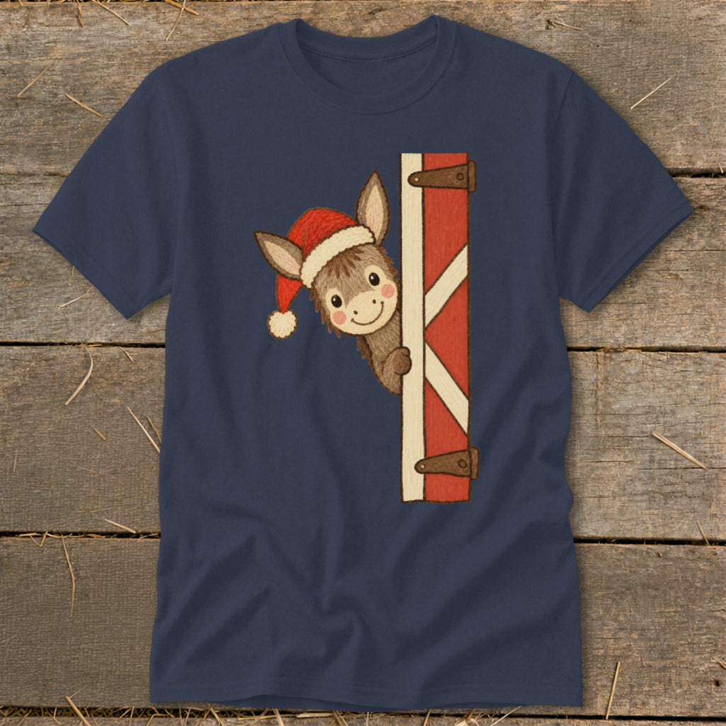 Donkey wearing Santa hat peeks around a red barn door on a navy t-shirt.