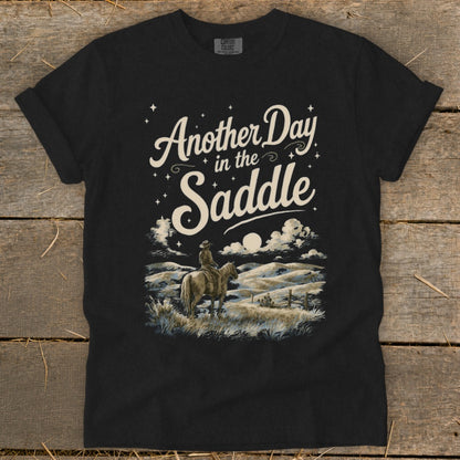 Black t-shirt with "Another Day in the Saddle" text above a ranch scene.