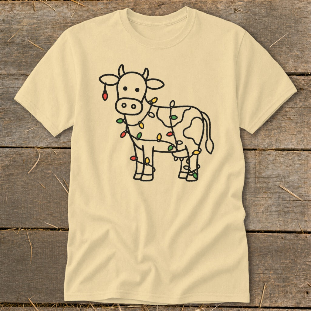 Light yellow t-shirt with a black outline drawing of a cow decorated with colorful Christmas lights.